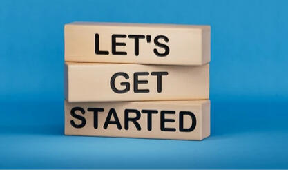 three wooden blocks that are stacked on each other. each block has one word. the top block says let;s, the middle block says get and the bottom block says started. background is light blue